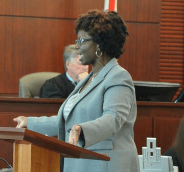 Regina Nunnally wearing a Blue t-shirt with the words "You should be Here" printed on the front and wearing sunglasses.
