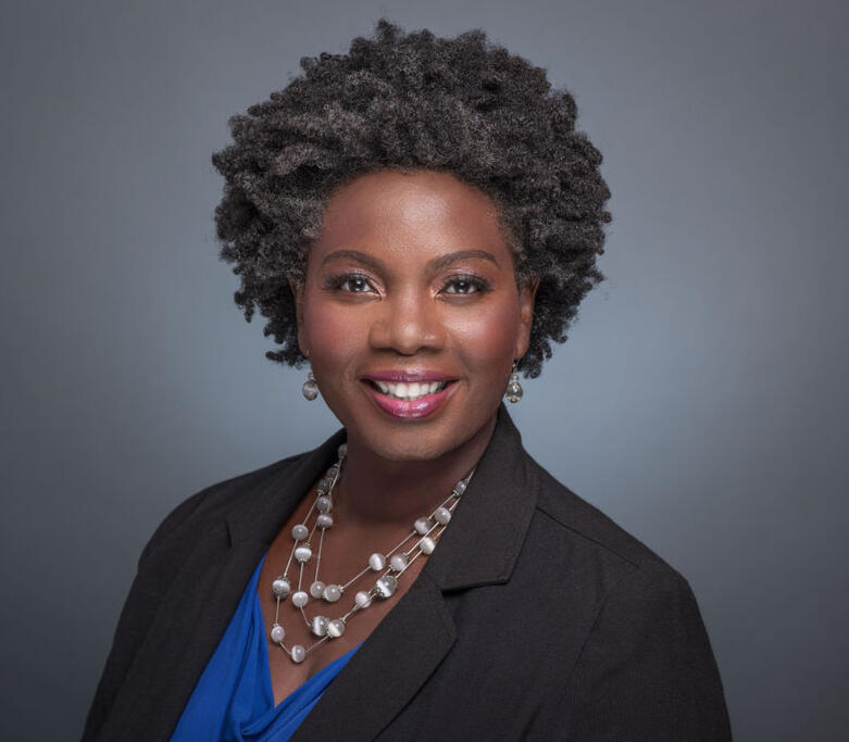 Headshot of Regina wearing a black suit and blue shirt